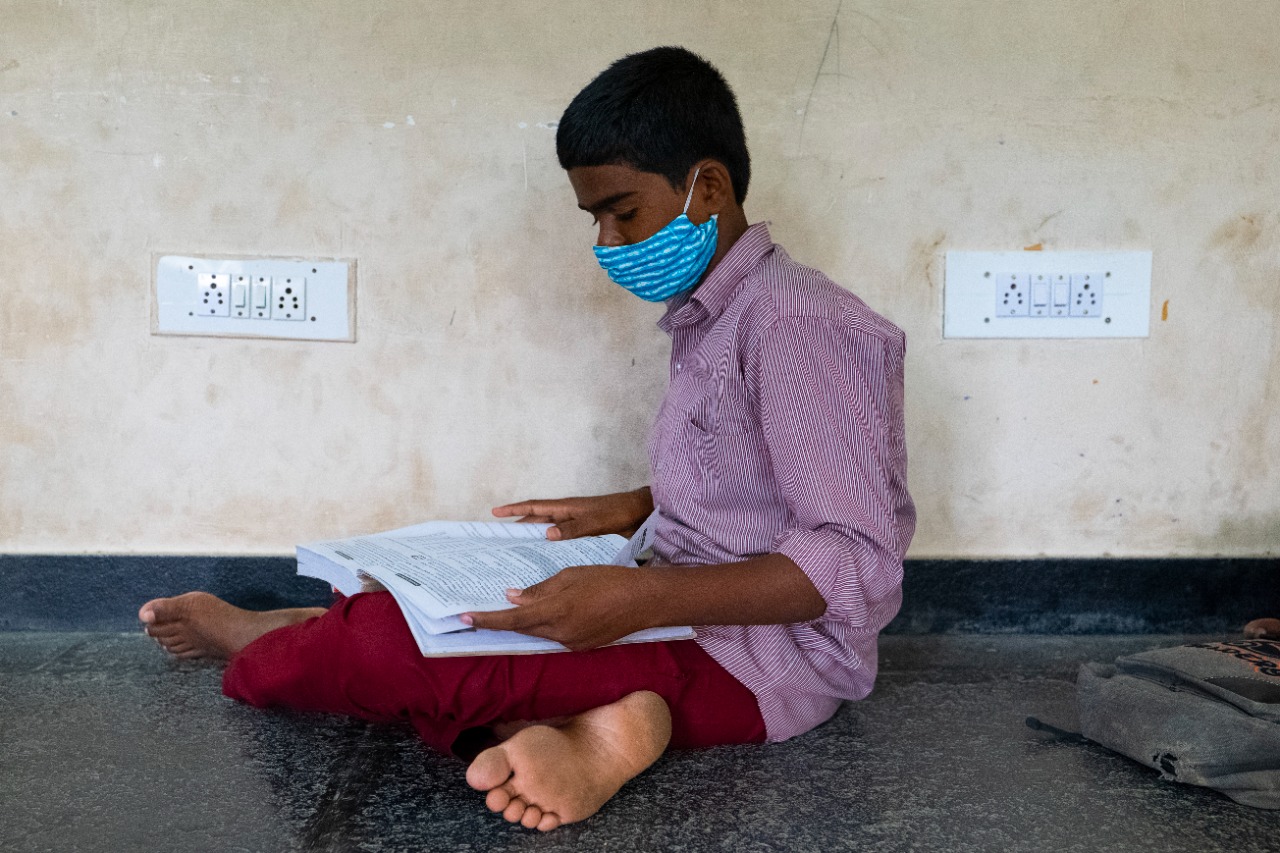 A boy sitting on the school house floor reading